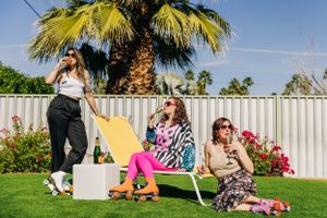 Three friends relax outdoors in Palm Springs with colorful chaise lounges, coolers and vibrant flowers in a backyard setting.