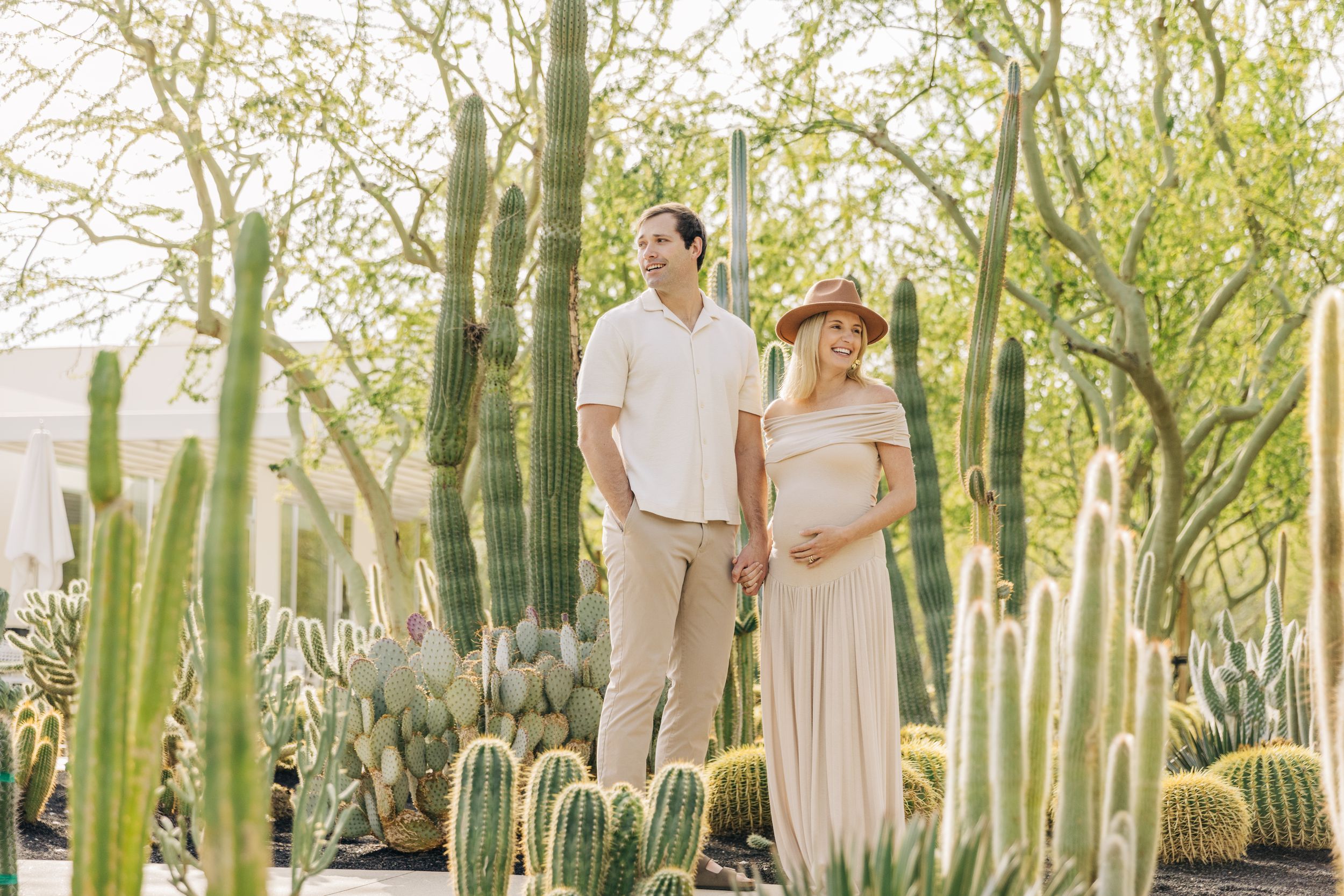 A couple poses for wedding photos in a lush desert garden surrounded by tall saguaro cacti and desert plants.