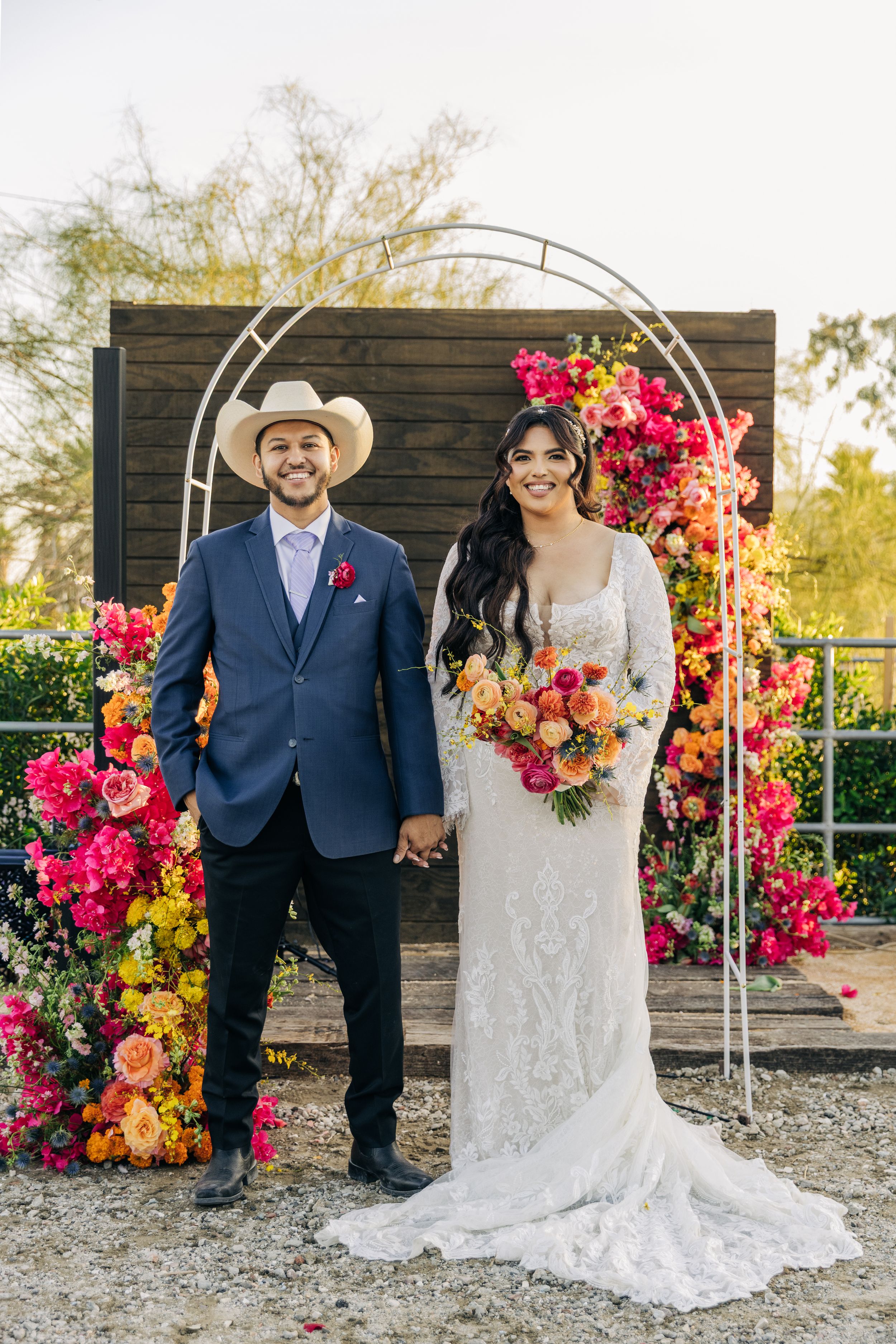 Romantic outdoor wedding portraits with vibrant pink and orange floral arrangements against rustic wooden backdrop.