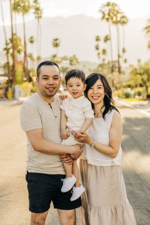 A family in coordinated beige and white outfits poses together on a palm tree-lined neighborhood in Palm Springs