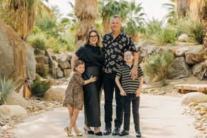 A family poses together in a desert landscape surrounded by palm trees and rocky terrain.