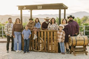 A group of people sitting together on a rustic wooden porch swing in a countryside setting.