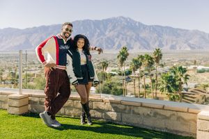 A couple shares a romantic moment with their dog against a scenic desert mountain backdrop with palm trees.