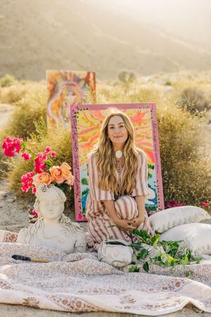 Boho styled outdoor photoshoot setup with patterned blanket, colorful frames, and pink flowers in desert landscape.