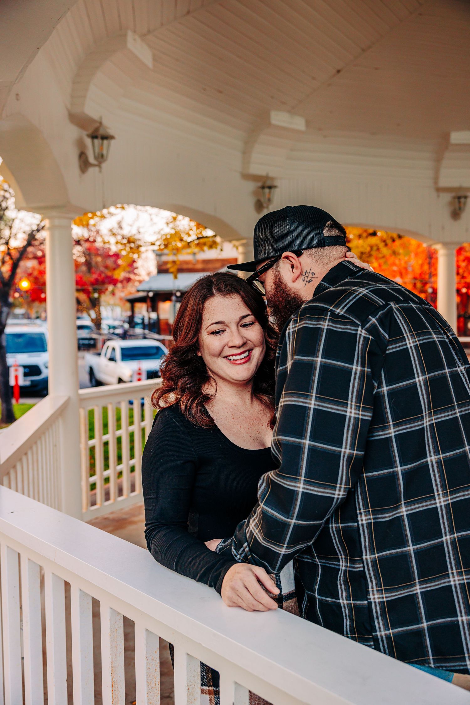 A couple shares intimate moments on a white porch railing during a fall engagement photoshoot.