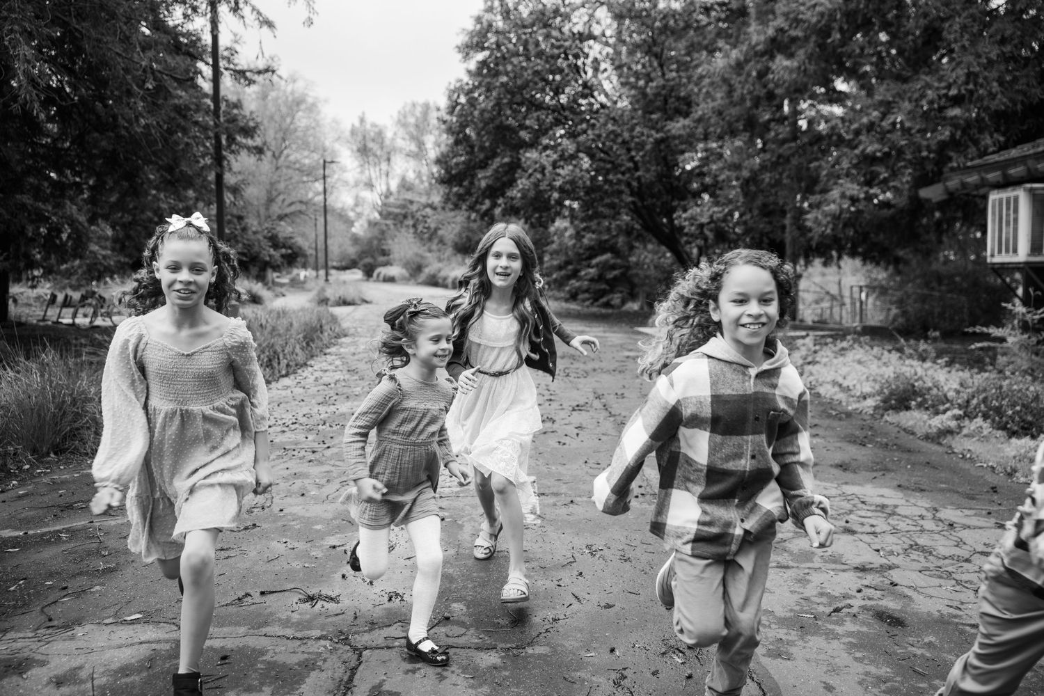 A series of black and white photos showing children playing and running together outdoors in a natural setting.