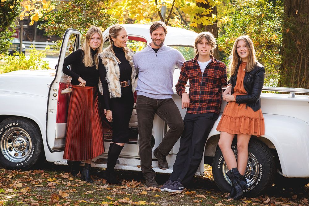 Group posed casually in front of vintage white truck during autumn season.