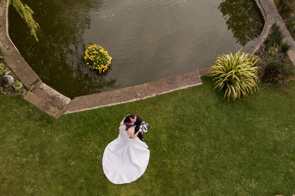 Aerial view of a wedding couple on manicured lawn near a waterfront setting.