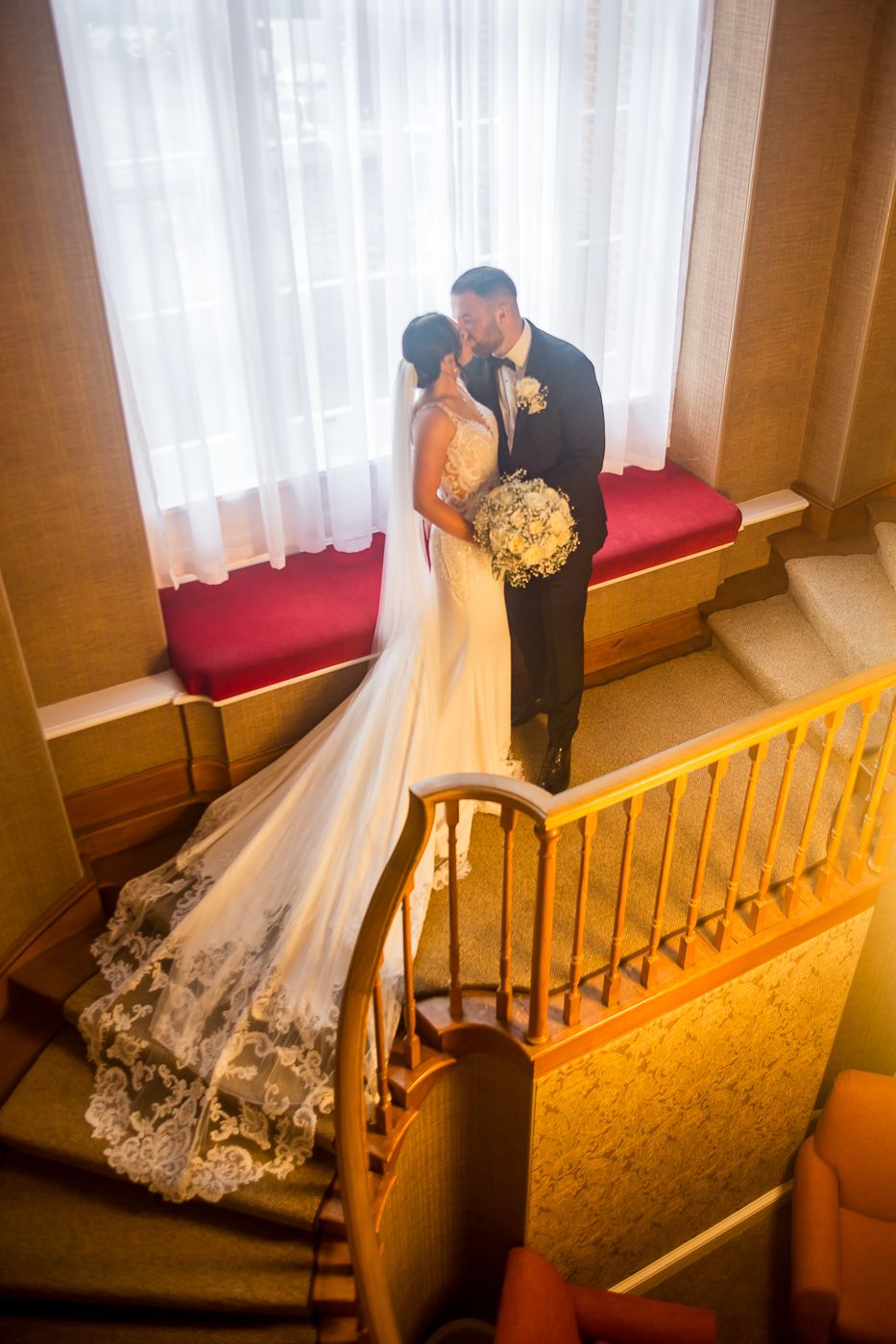 Wedding couple on wooden staircase with dramatic lighting and flowing white dress.