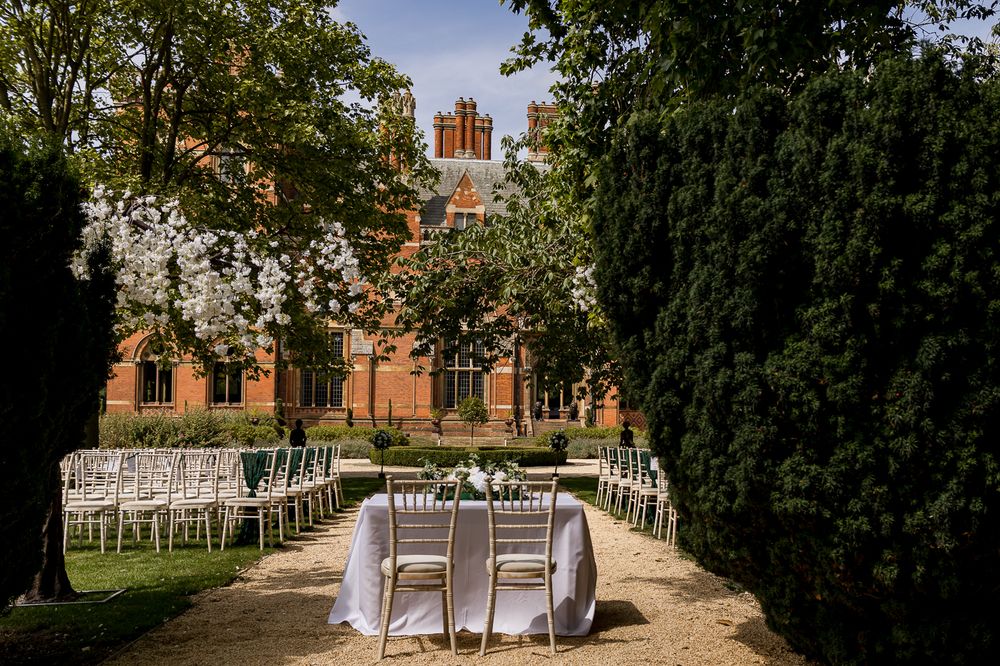 Wedding ceremony setup outdoors with white chairs and brick building backdrop in natural setting.