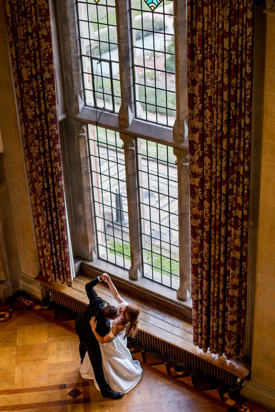 Dramatic window light indoor wedding photos with vintage curtains and wooden floors.