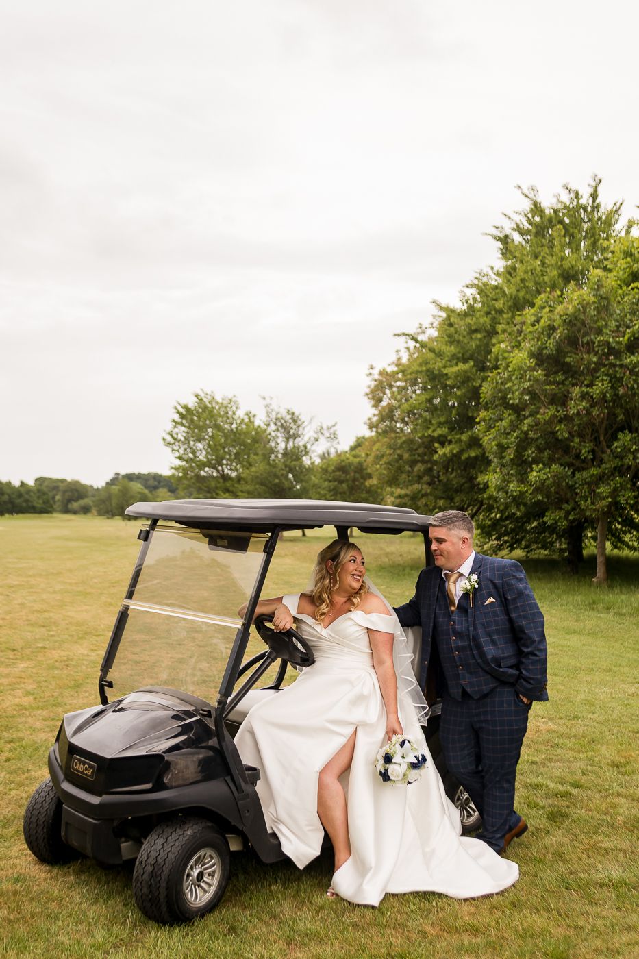 Wedding couple posing with a golf cart on a sunny meadow.
