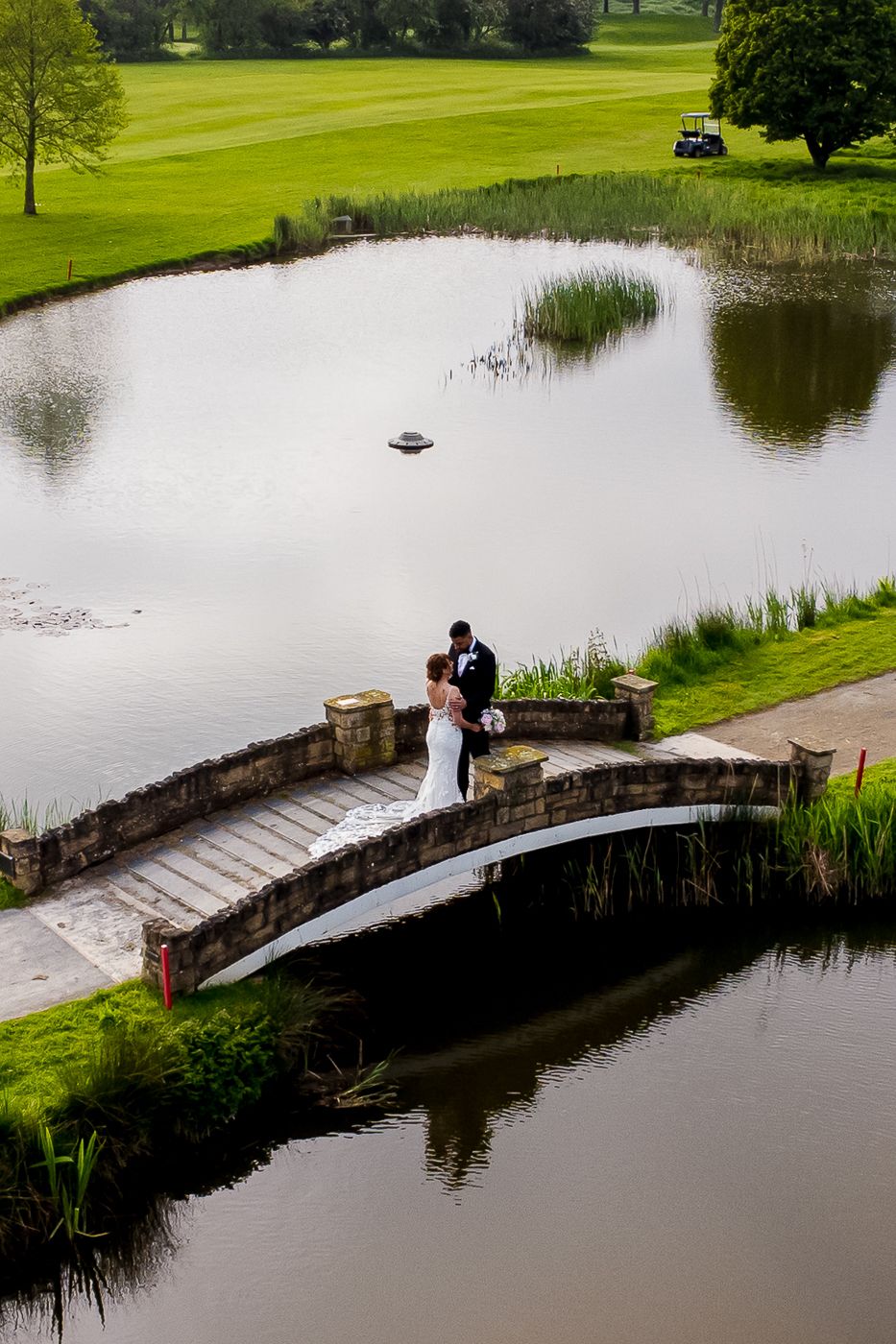 Scenic golf course wedding venue with a curved stone bridge over a tranquil pond.