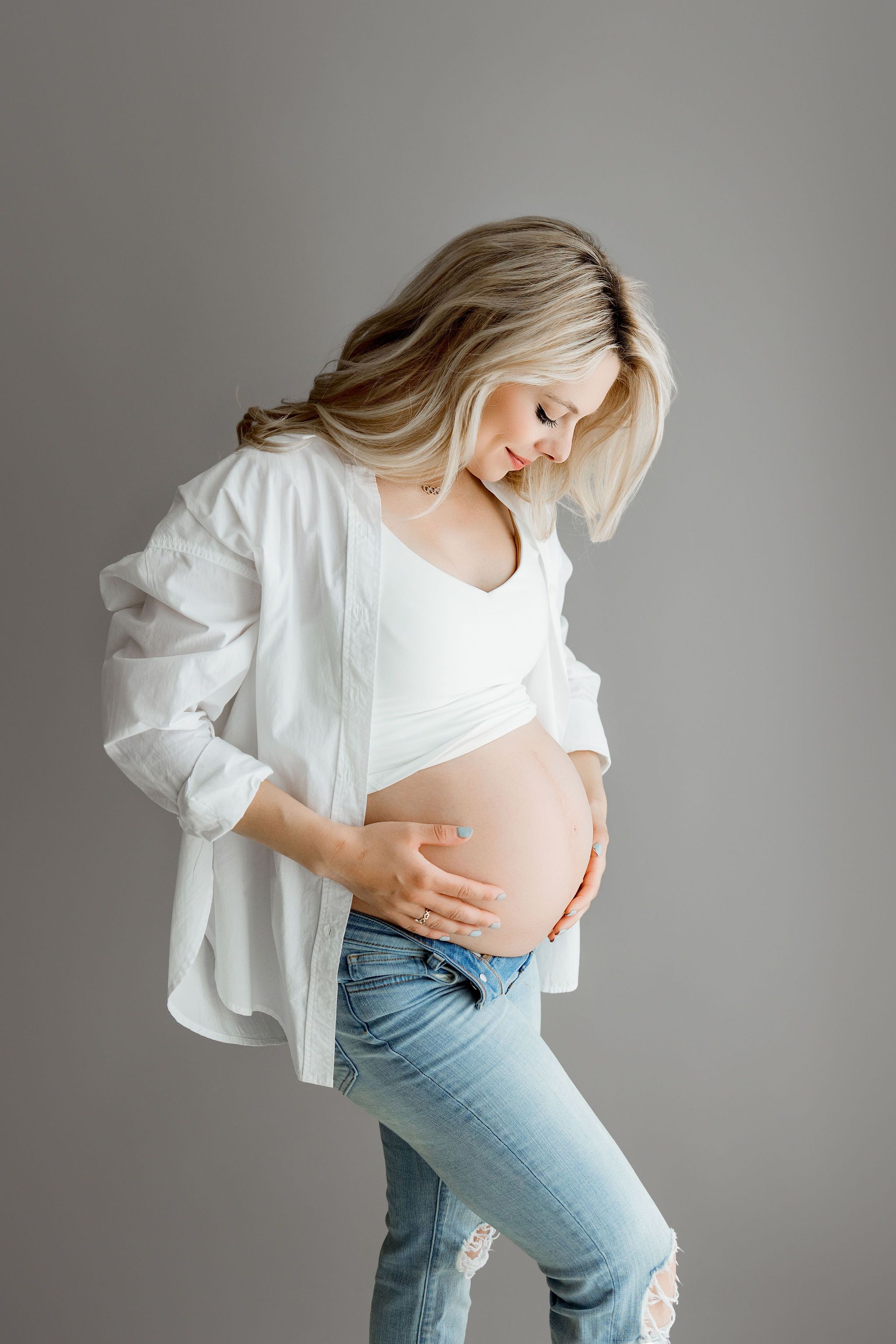 Pregnancy photo on a gray backdrop, mom wearing jeans and white shirt, Algonquin IL maternity newborn photographer