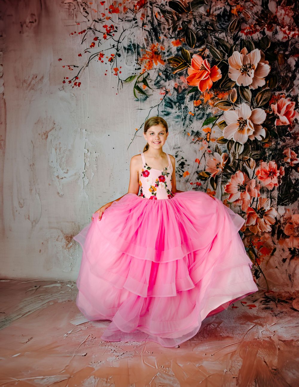 Dream Dress Studio Broken Arrow backdrop is peach floral textured with tween in a pink ruffle dress with tulle and dream dress couture gown
