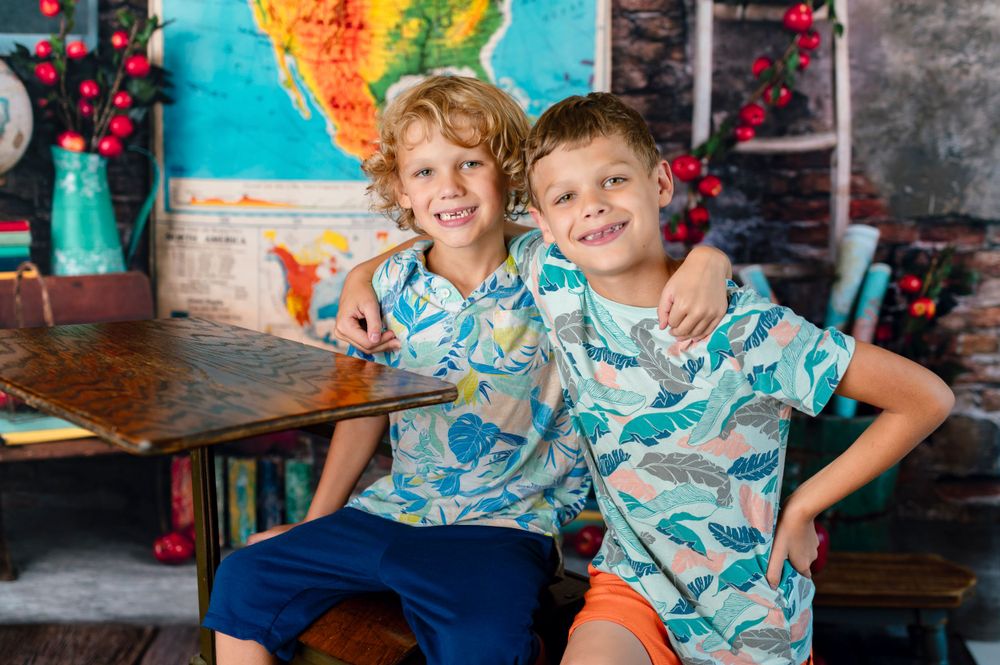 back to school indoor photography session in broken arrow oklahoma with elementary aged brothers and a desk with map background and apples