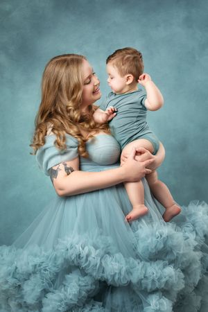 A tender moment captured between parent and child in matching teal outfits against a dreamy turquoise backdrop.