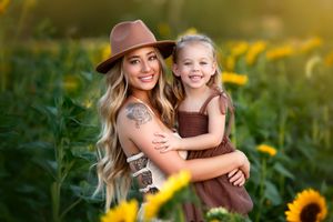 Mother and daughter share a joyful embrace in a golden sunflower field at sunset.
