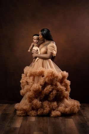 A sweeping ethereal portrait in brown tones featuring a flowing peach tulle gown against a dark studio backdrop.