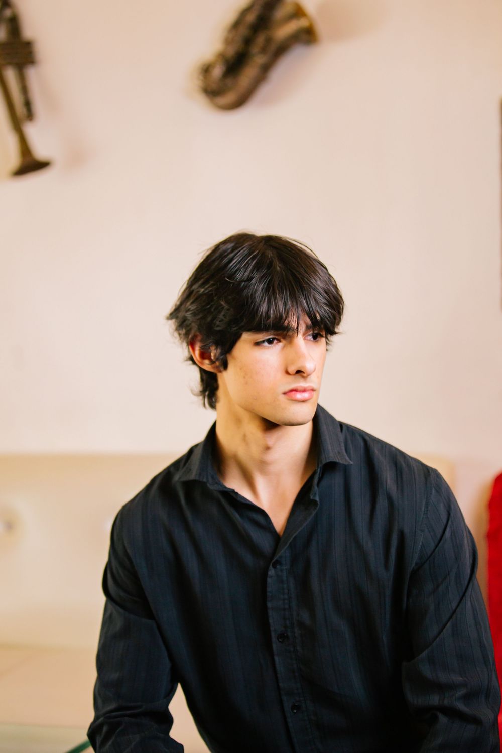 Person in black shirt sitting against beige wall in a candid photo series.