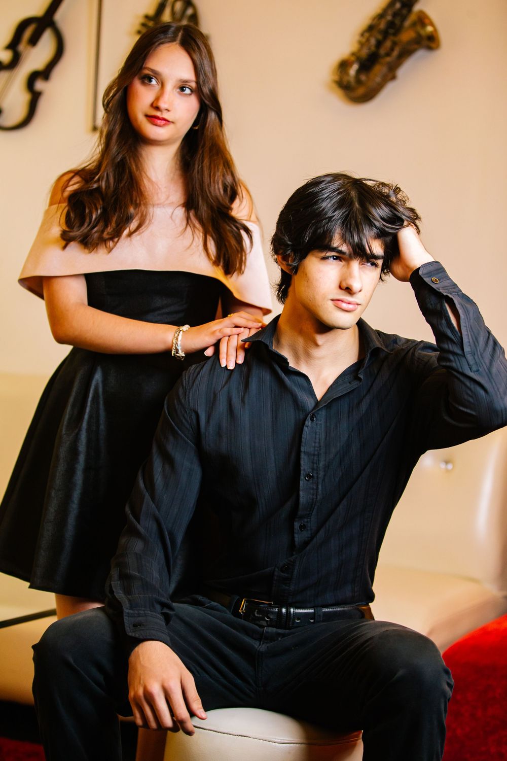A fashion photo series showing a person in black clothing posing on a red couch against a beige wall.