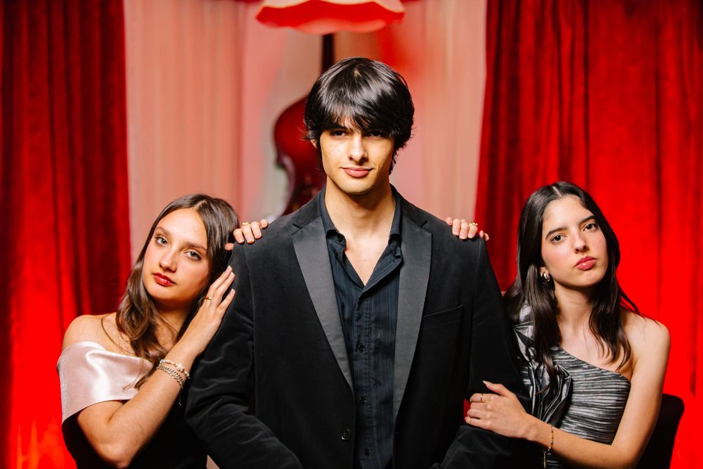 Group of performers posing together against a red curtain backdrop in formal attire.