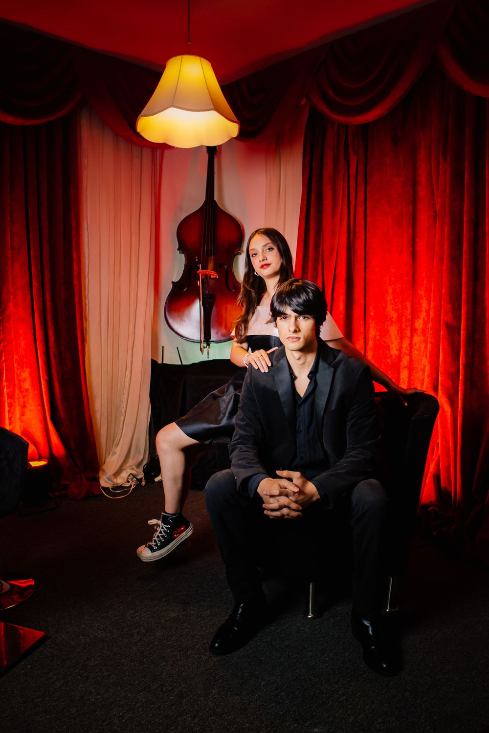 A moody series of photos showing people seated in a dark room with red curtains and dramatic lighting from a table lamp.