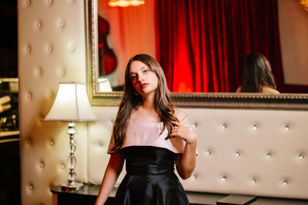 Woman in red dress poses elegantly on tufted white sofa in glamorous interior setting.