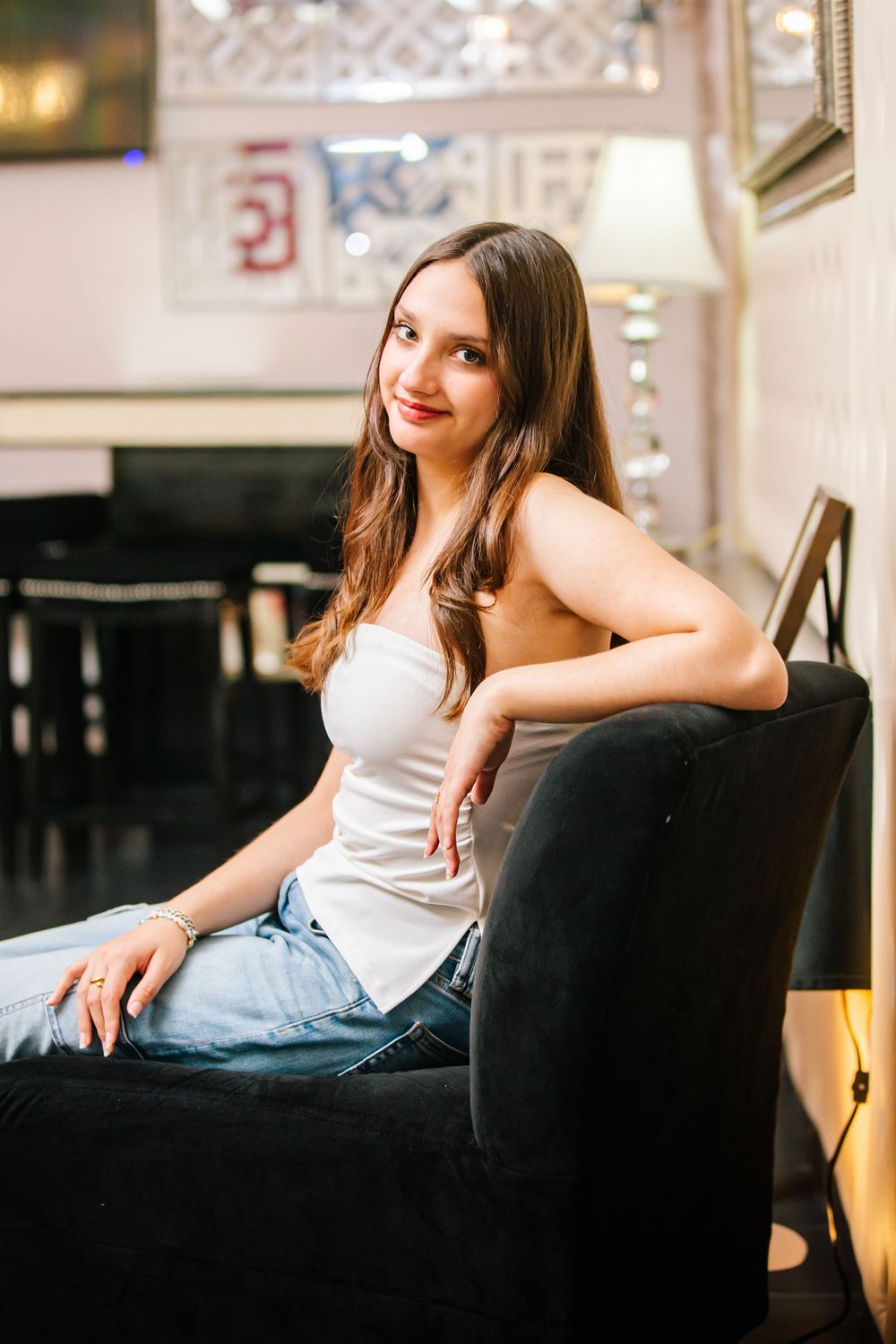 A person in casual attire lounges on a black leather couch in a well-lit interior setting.
