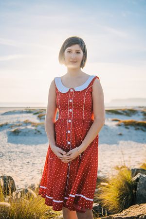 Young woman in red polka dot dress standing on sandy beach at golden hour.