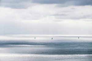 Three sailboats on a calm silver sea under dramatic cloudy sky.