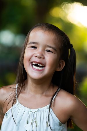 Young girl with pigtails laughing joyfully outdoors in white dress with bokeh background.