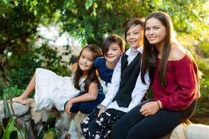 Four siblings posing together outdoors in a lush green garden setting.