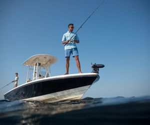 Man standing on bow of center console boat fishing in open ocean waters on a clear sunny day.