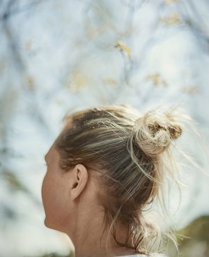 Close-up back view of blonde woman with messy bun and hair accessories outdoors.