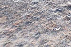 Abstract texture of shallow ocean water washing over sandy beach shore.