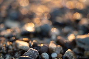 Close-up of smooth pebbles on a beach with golden bokeh light in the background.