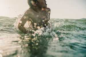 Woman emerging from sparkling sunlit ocean water with bokeh light effects.