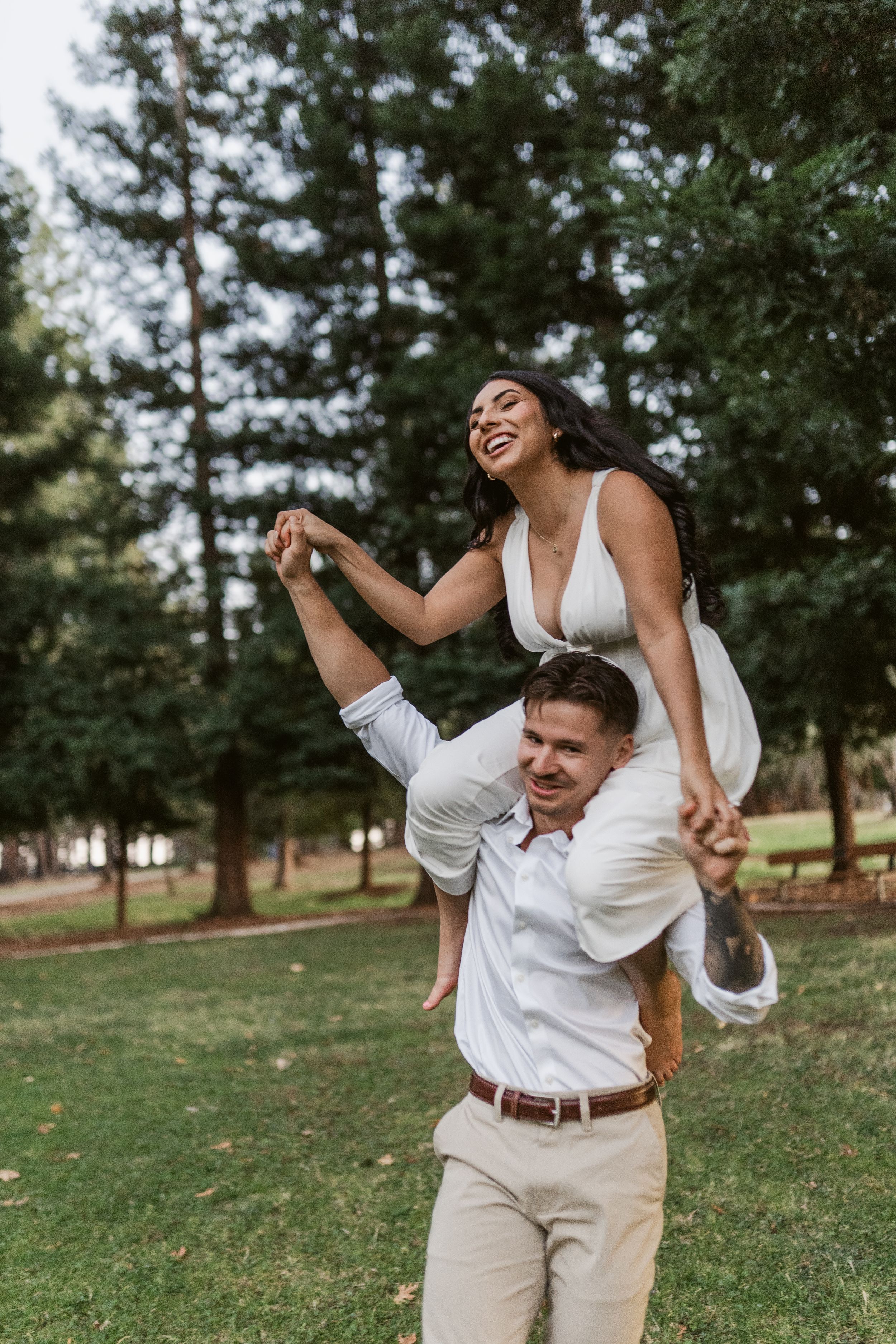 A joyful couple dances and twirls playfully together on a grassy lawn with pine trees in the background.