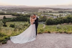 Ein Hochzeitspaar posiert bei Sonnenuntergang vor einem malerischen Blick auf die Landschaft.