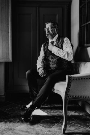 Ein stimmungsvolles Schwarz-Weiß-Porträt eines Gentleman in Vintage-Kleidung, der auf einem eleganten Stuhl sitzt.
