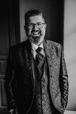 Klassisches Schwarz-Weiß-Porträt mit einem fröhlichem Gentleman in einer gemusterten Anzugjacke und Brille.