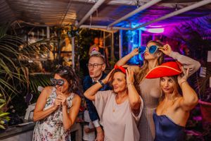 Hochzeitsparty-Gäste tanzen und feiern unter bunter lila Beleuchtung bei einem Innenempfang.