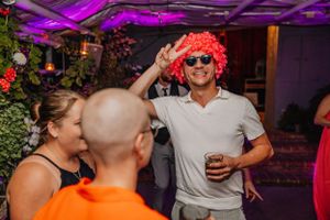 Partygäste feiern mit festlichen Requisiten unter lila Stimmungsbeleuchtung bei einer Indoor-Veranstaltung.
