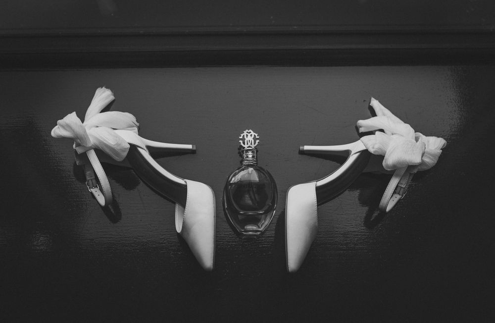Black and white close-up of gloved hands holding perfume bottles against dark background. Mill Barns