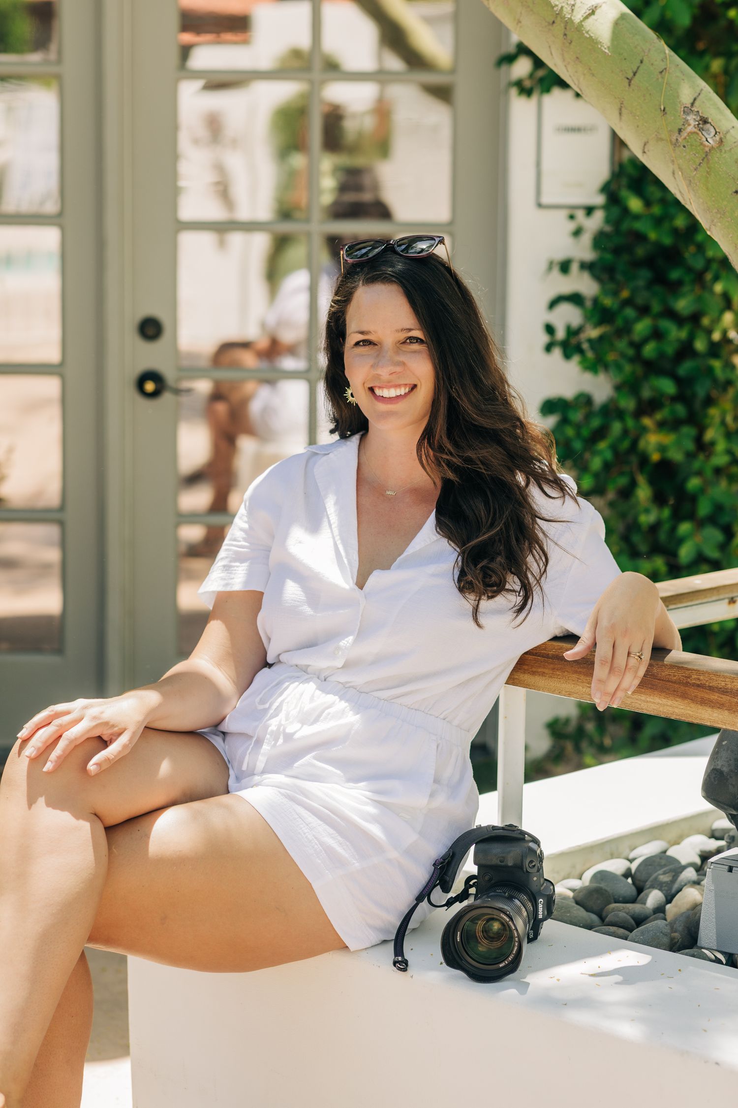 Woman in white button-down shirt relaxes on outdoor patio furniture with camera in warm natural lighting.
