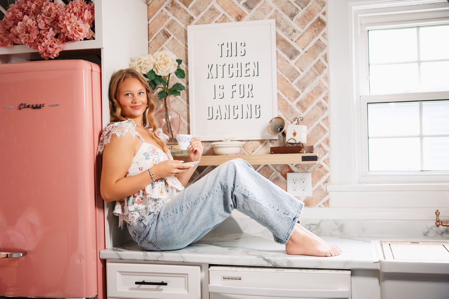 A bright modern kitchen interior with white subway tile backsplash, coral pink walls and natural light streaming in.