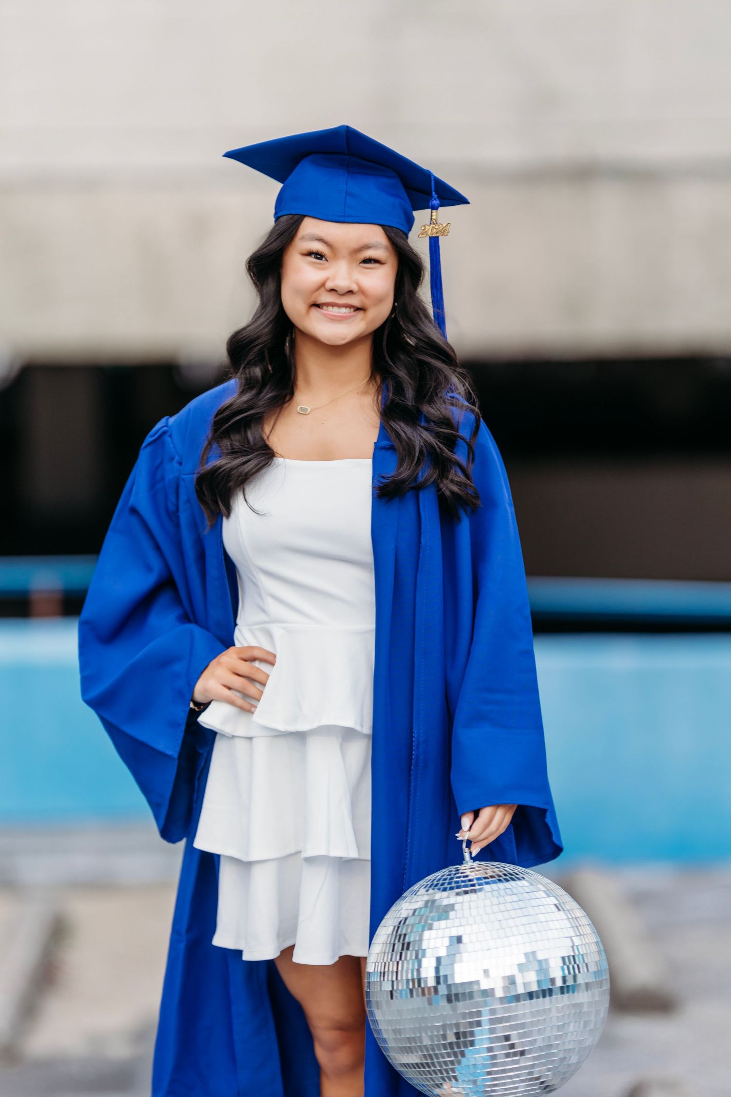 Graduate in blue cap and gown holding disco ball against urban backdrop. Middle TN Senior photographer