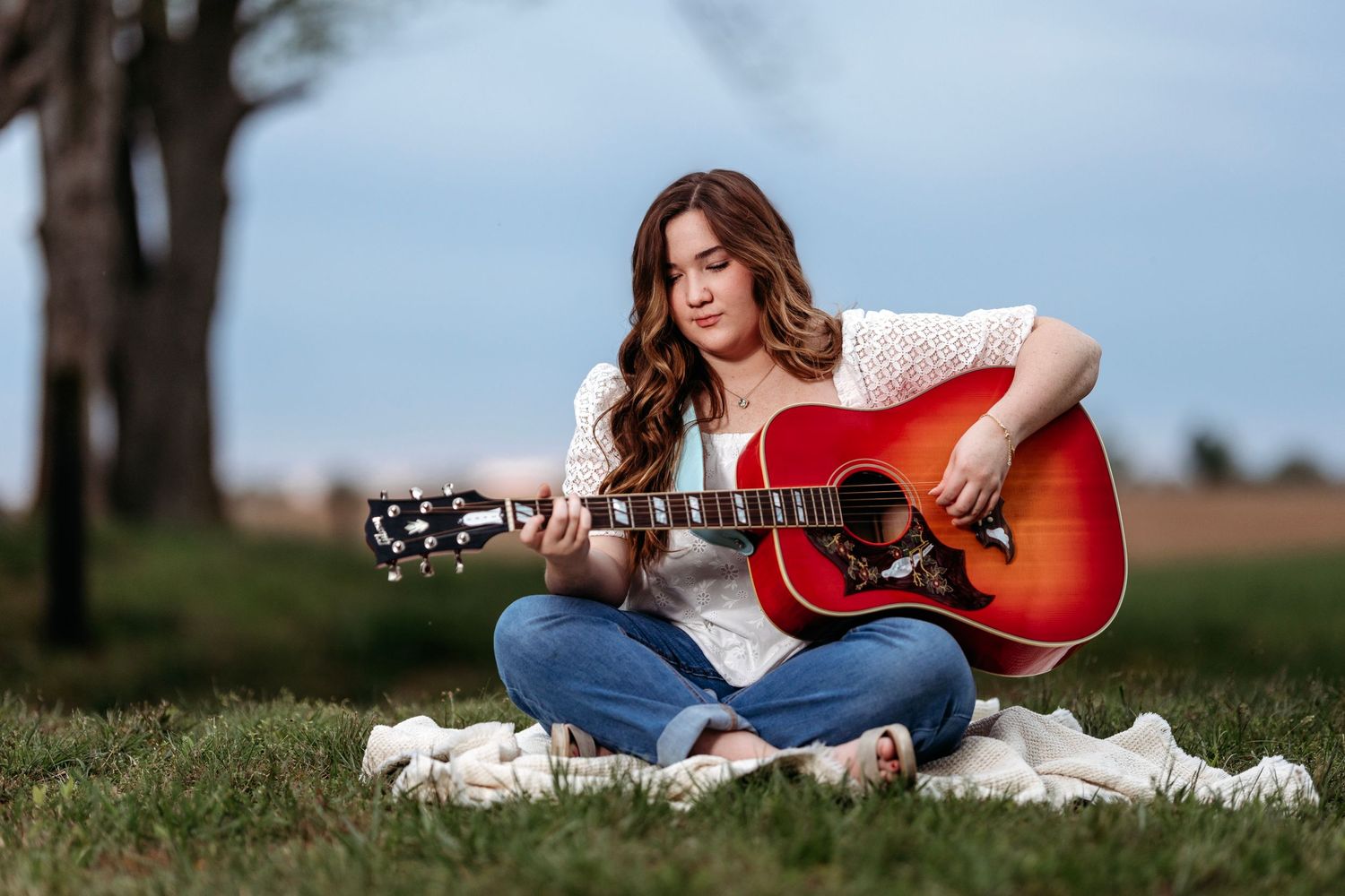 senior girl in casual attire playing acoustic guitar while sitting on blanket in grassy field. Middle TN Senior photographer