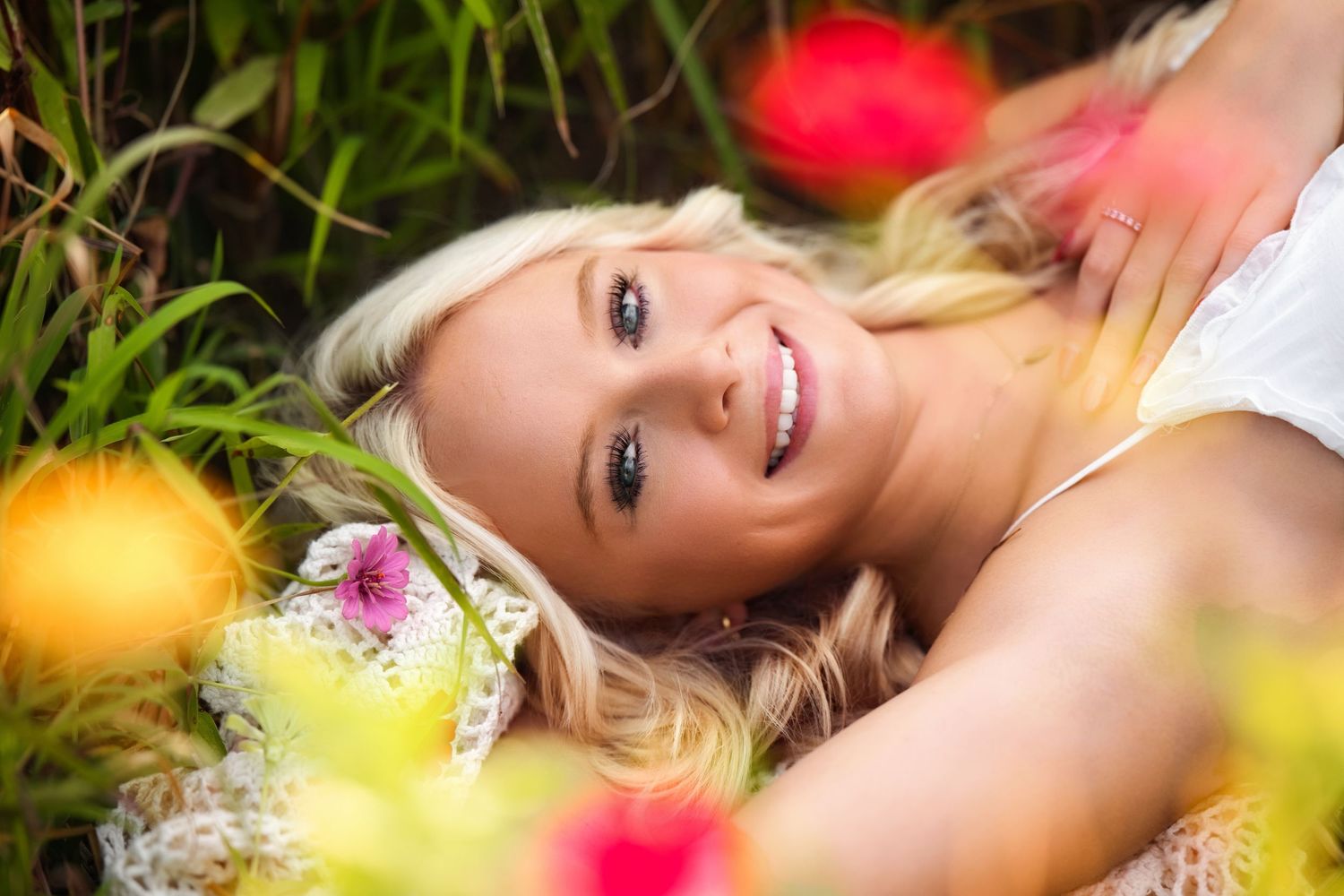 A person lies in a garden surrounded by vibrant red and yellow flowers on a sunny day.
